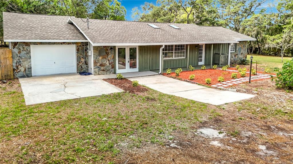 A single-story house features a stone facade, a white garage door, and a green exterior — 13206 TYRONE STREET, HUDSON, FL