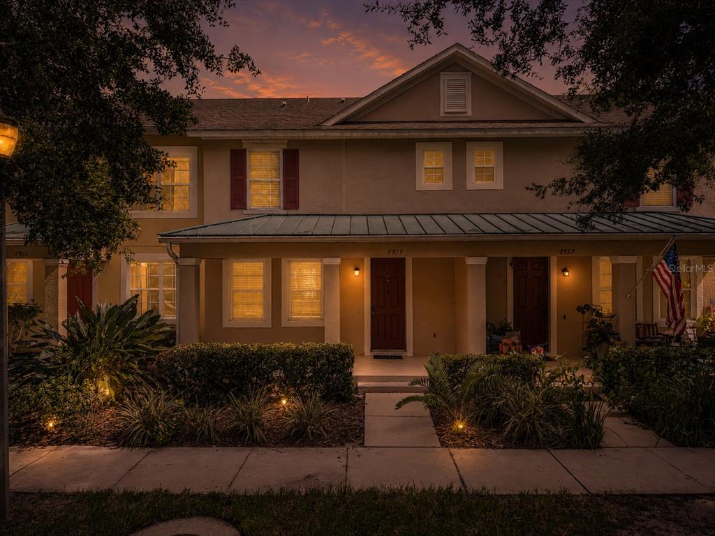 A two-story townhouse exterior with a covered front porch and warm evening lighting — 7919 NORTHLAKE PARKWAY, ORLANDO, FL