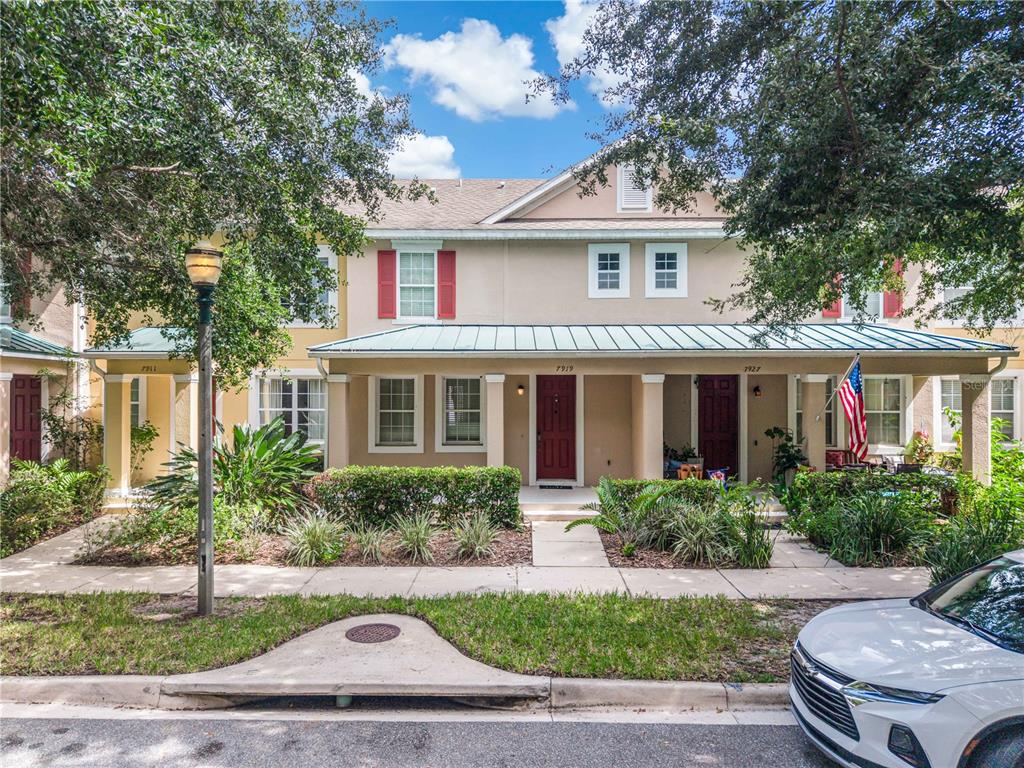 A row of townhouses with beige stucco walls, red shutters, and a shared metal porch roof — 7919 NORTHLAKE PARKWAY, ORLANDO, FL