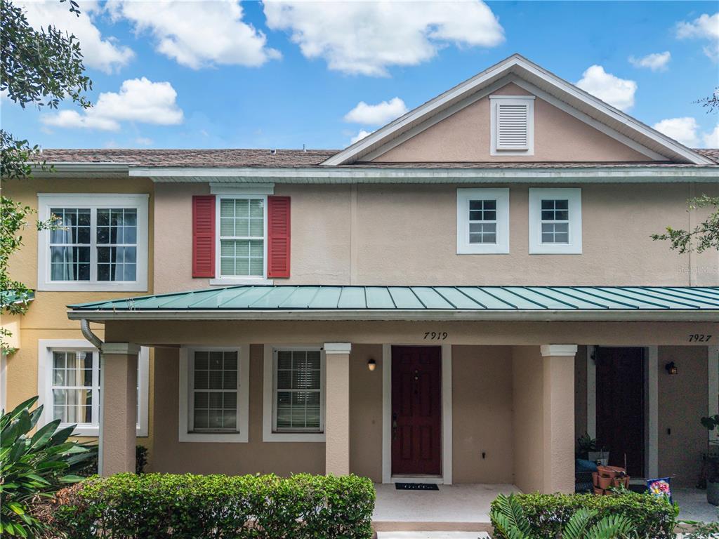A two-story townhouse with a tan stucco exterior, a green metal porch roof, and red shutters — 7919 NORTHLAKE PARKWAY, ORLANDO, FL