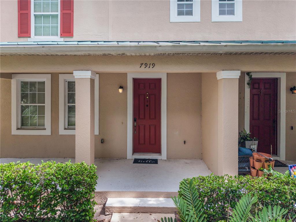 The exterior of a tan two-story townhouse features two red front doors and a porch — 7919 NORTHLAKE PARKWAY, ORLANDO, FL