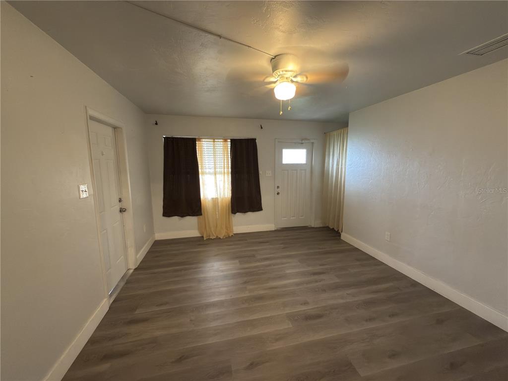 An empty room features gray wood-look flooring, white walls, a ceiling fan, and two doors — 8274 BUMFORD AVENUE, NORTH PORT, FL
