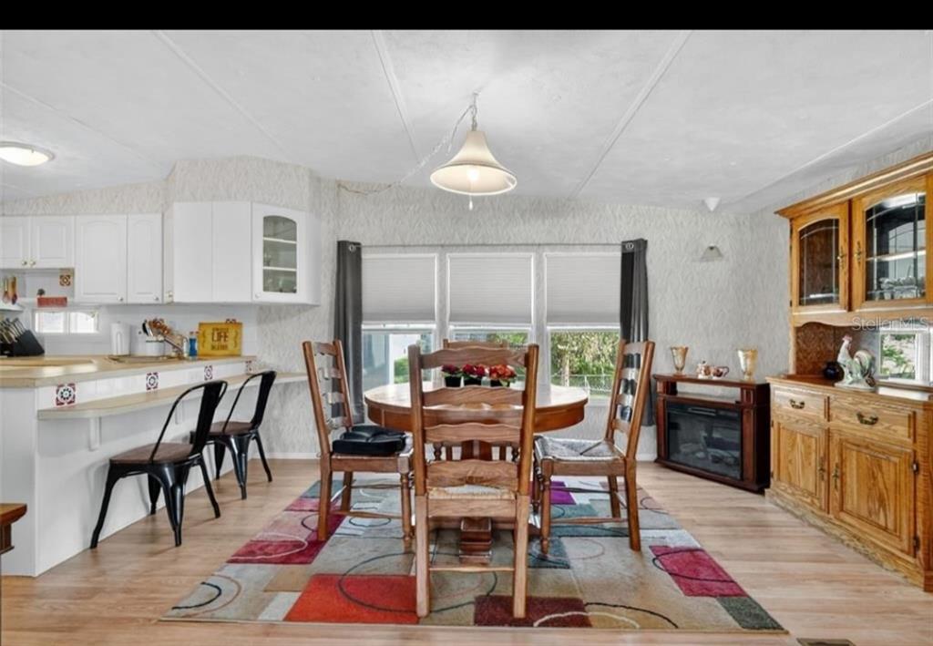 A dining area with a wooden table, chairs, a colorful rug, and a kitchen breakfast bar — 11905 LINDA AVENUE, TAVARES, FL