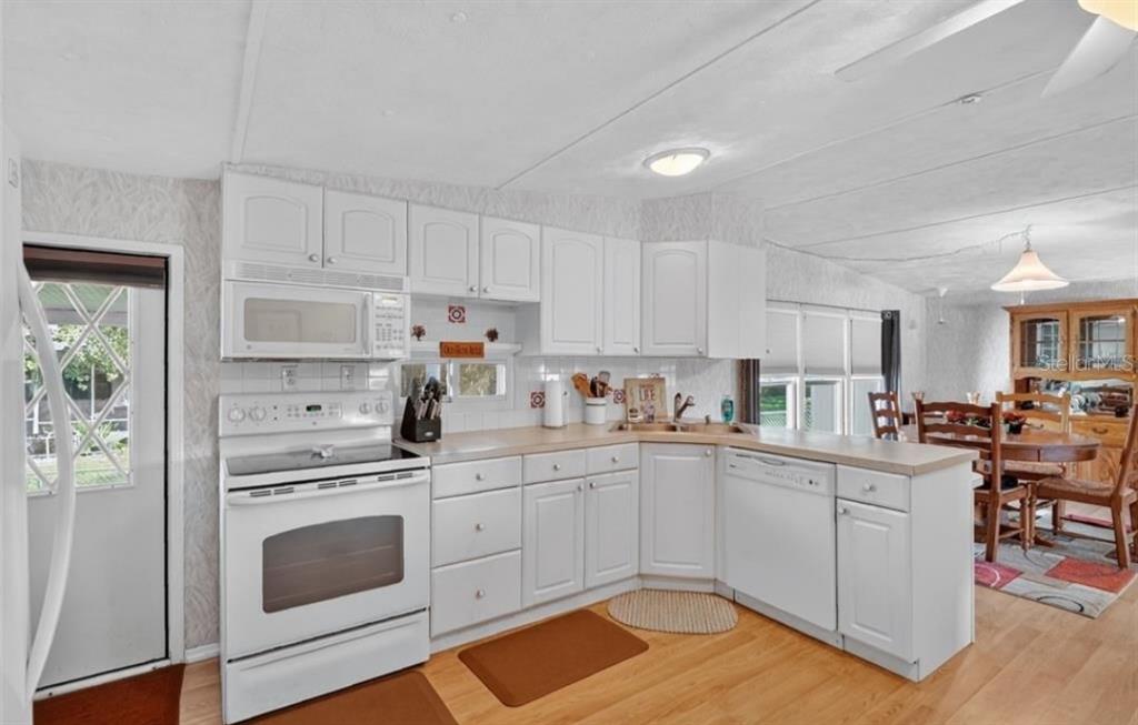 A kitchen with white cabinets, white appliances, and light wood flooring opens to a dining area — 11905 LINDA AVENUE, TAVARES, FL