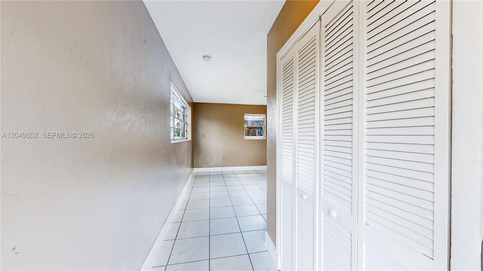 A hallway with white tile flooring leads to a room with brown walls — 2760 NW 58th St, Miami FL 33142, MIAMI, FL