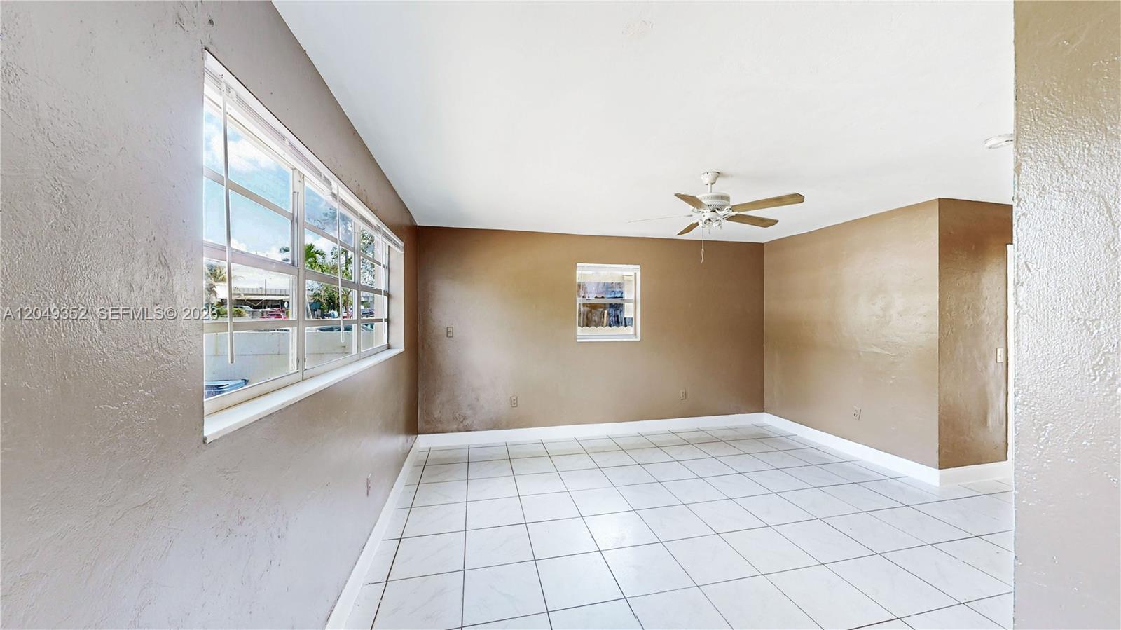 An empty room features brown walls, white tile flooring, a ceiling fan, and large windows — 2760 NW 58th St, Miami FL 33142, MIAMI, FL