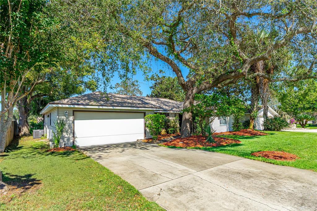 A single-story house with a white garage door, concrete driveway, and large mature trees — 693 REILLYS ROAD, PORT ORANGE, FL