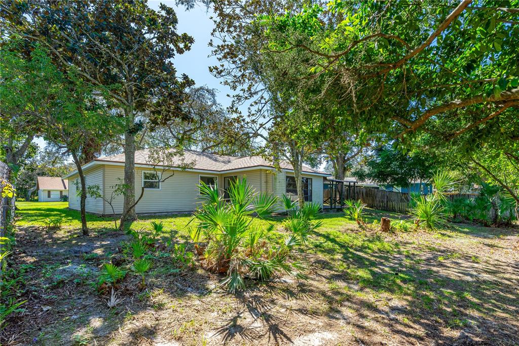 The exterior of a single-story house with light-colored siding is surrounded by trees and vegetation — 693 REILLYS ROAD, PORT ORANGE, FL