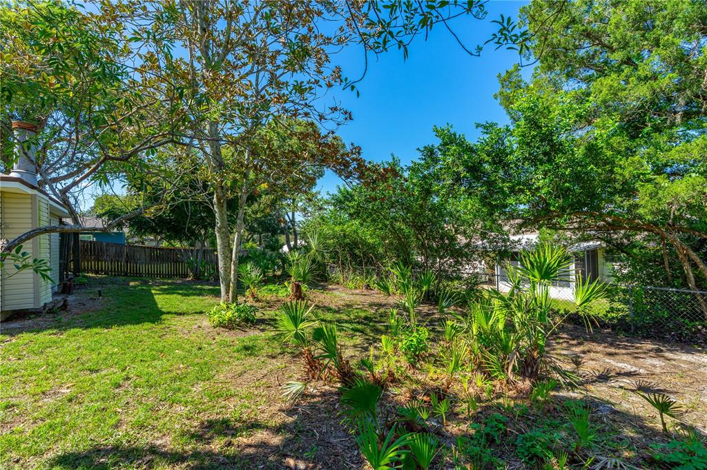A grassy backyard features mature trees, small palm plants, and a wooden fence — 693 REILLYS ROAD, PORT ORANGE, FL
