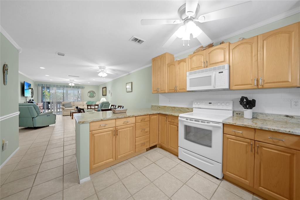 A kitchen with light wood cabinets, granite countertops, and white appliances opens to a living area — 1636 STICKNEY POINT ROAD UNIT 36-201, SARASOTA, FL