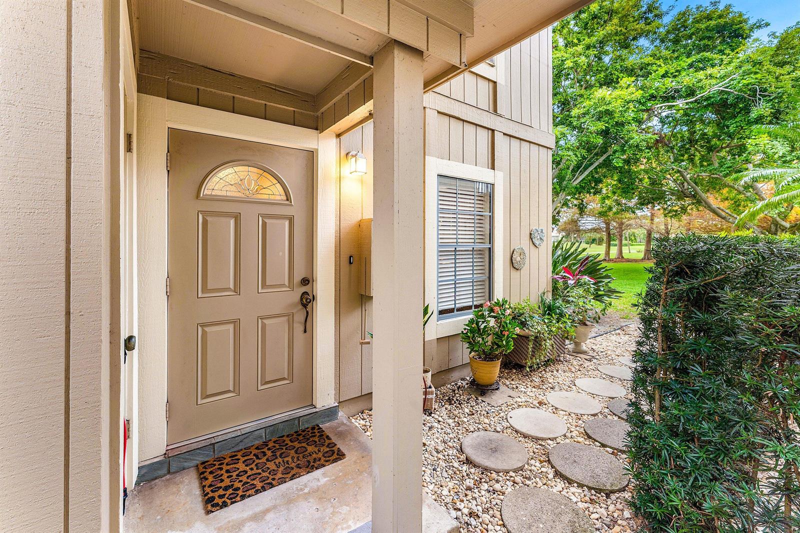 A tan front door with a glass insert sits under a covered porch with landscaping — 9179 SE Riverfront Terrace # F, Jupiter FL 33469, JUPITER, FL