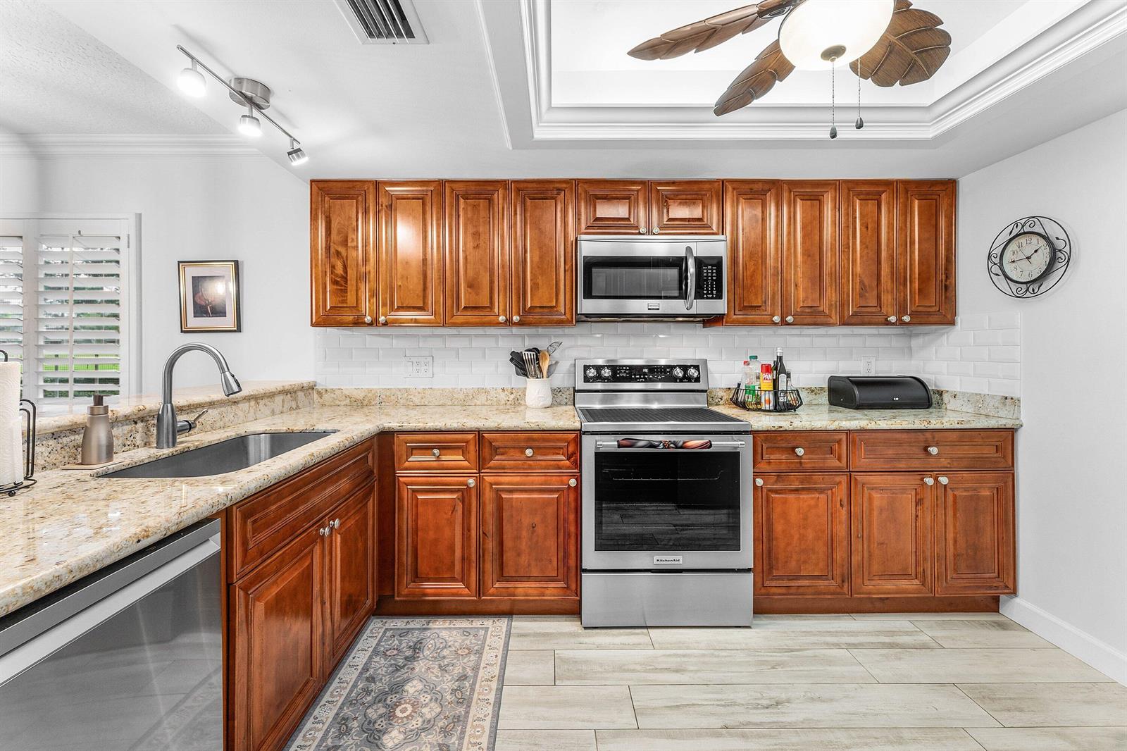 A kitchen features wood cabinets, granite countertops, stainless steel appliances, and a subway tile backsplash — 9179 SE Riverfront Terrace # F, Jupiter FL 33469, JUPITER, FL