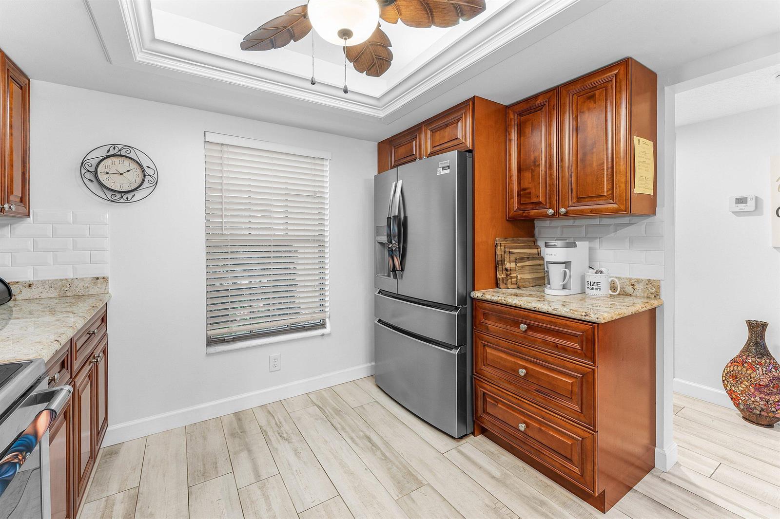 A kitchen features wood cabinets, granite countertops, stainless steel appliances, and light-colored wood-look tile flooring — 9179 SE Riverfront Terrace # F, Jupiter FL 33469, JUPITER, FL