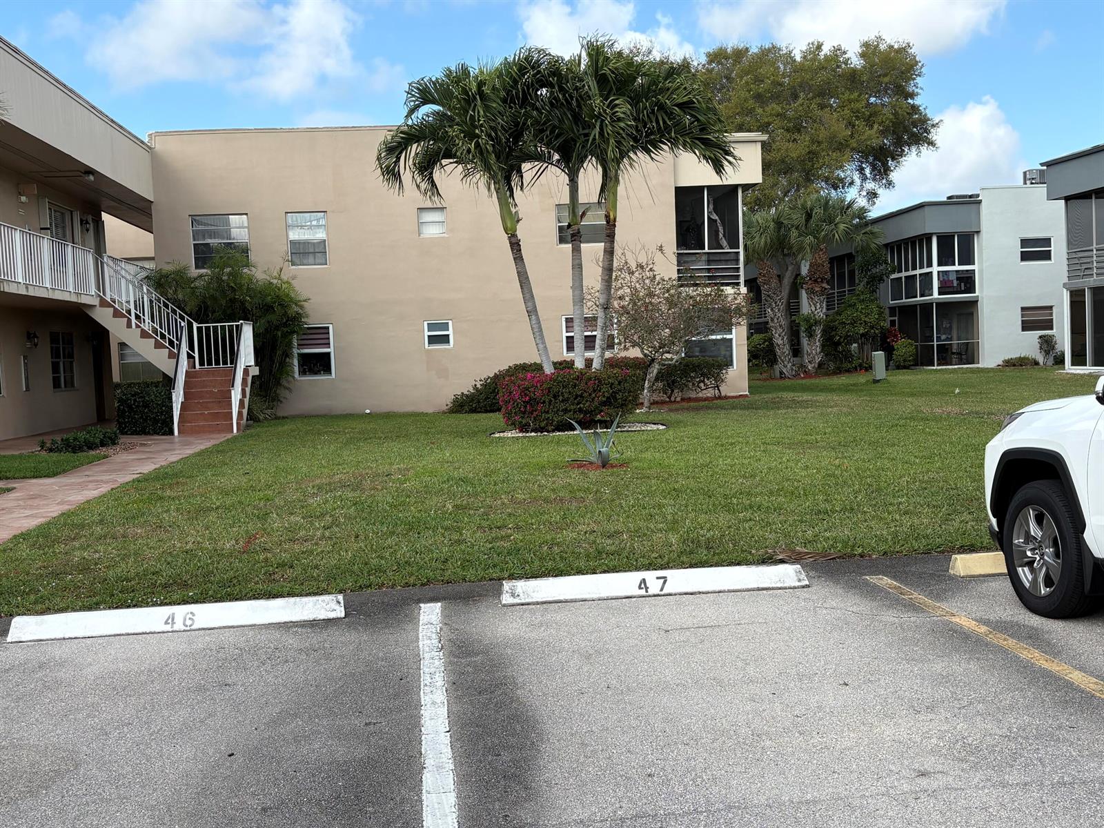 A tan apartment building exterior features a staircase, palm trees, and numbered parking spaces — 862 Normandy R Trail # R, Delray Beach FL 33484, DELRAY BEACH, FL
