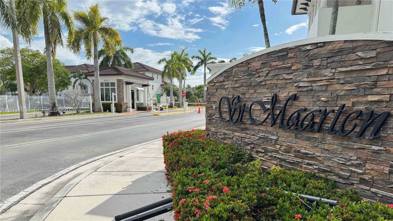 A stone monument sign for St. Maarten stands beside a road with palm trees — DORAL, FL