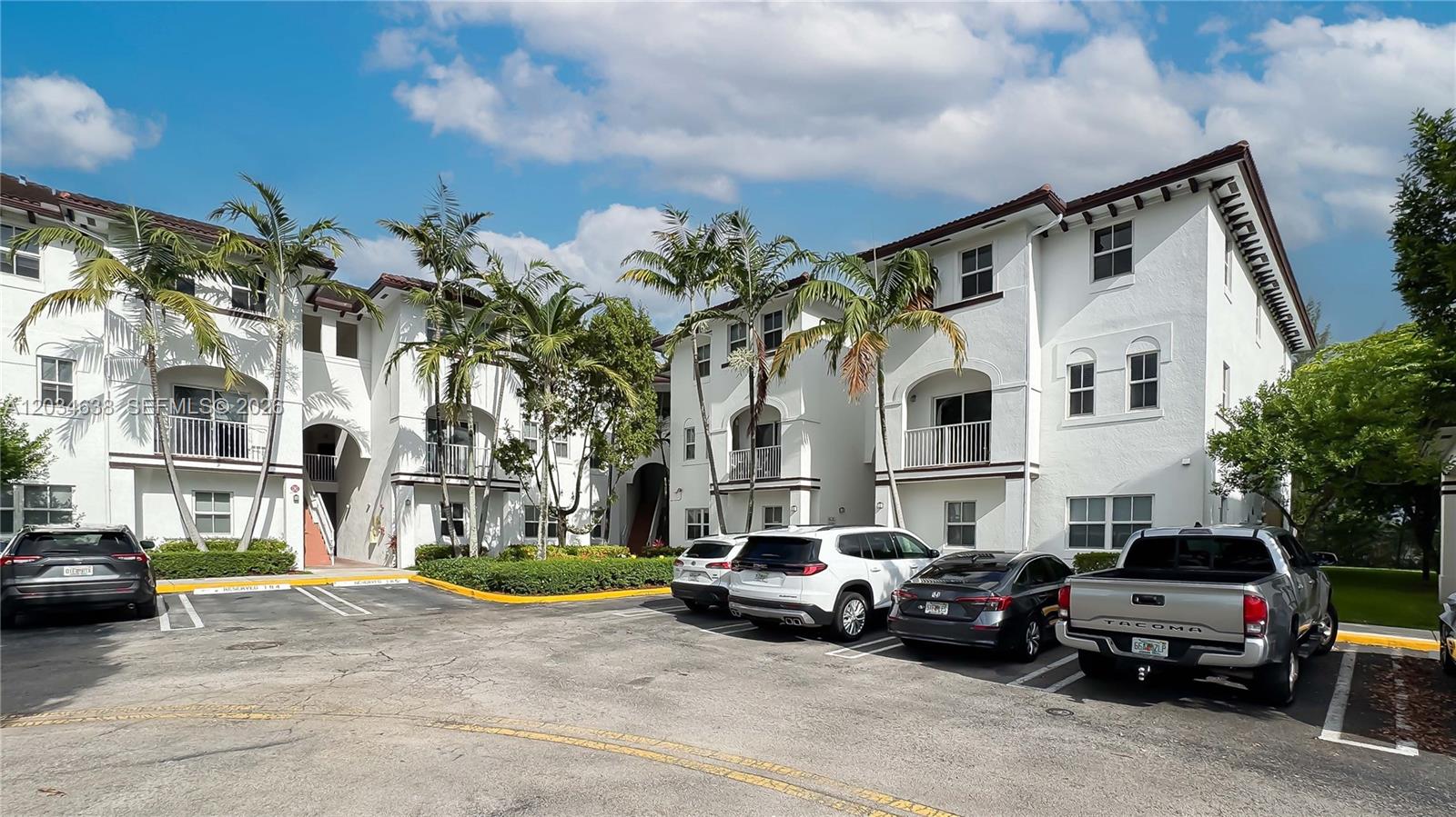 A multi-story white apartment building with palm trees and a parking lot in front — DORAL, FL