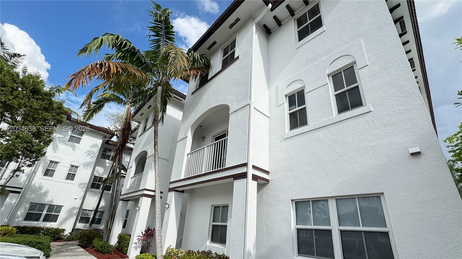 A low-angle exterior view of a white multi-story residential building with palm trees — DORAL, FL