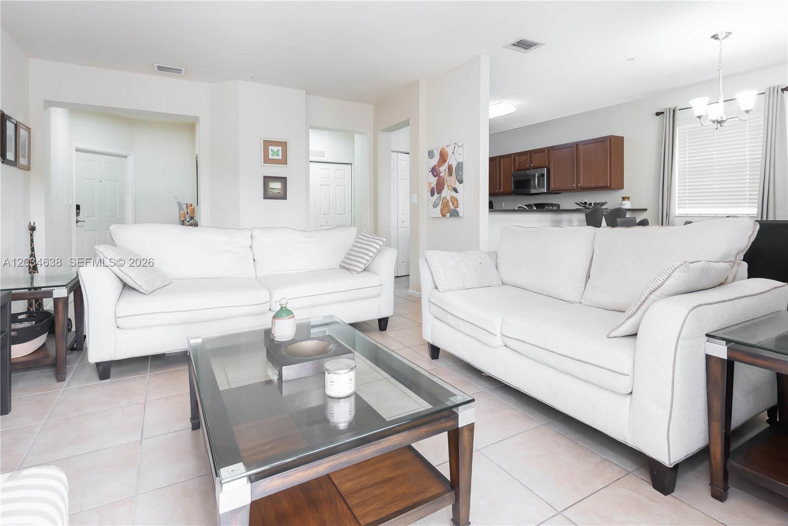 A living room features two white sofas, a glass coffee table, and an adjacent kitchen — DORAL, FL