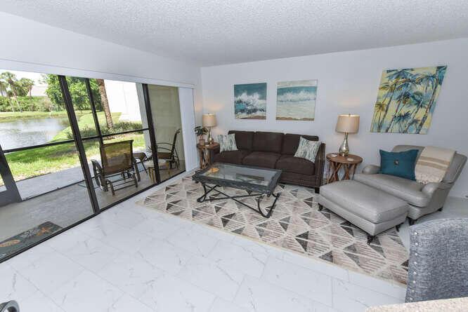 A living room features a brown sofa, gray armchair with ottoman, and sliding doors to a patio — 1605 S Us Highway 1 # B105, Jupiter FL 33477, JUPITER, FL