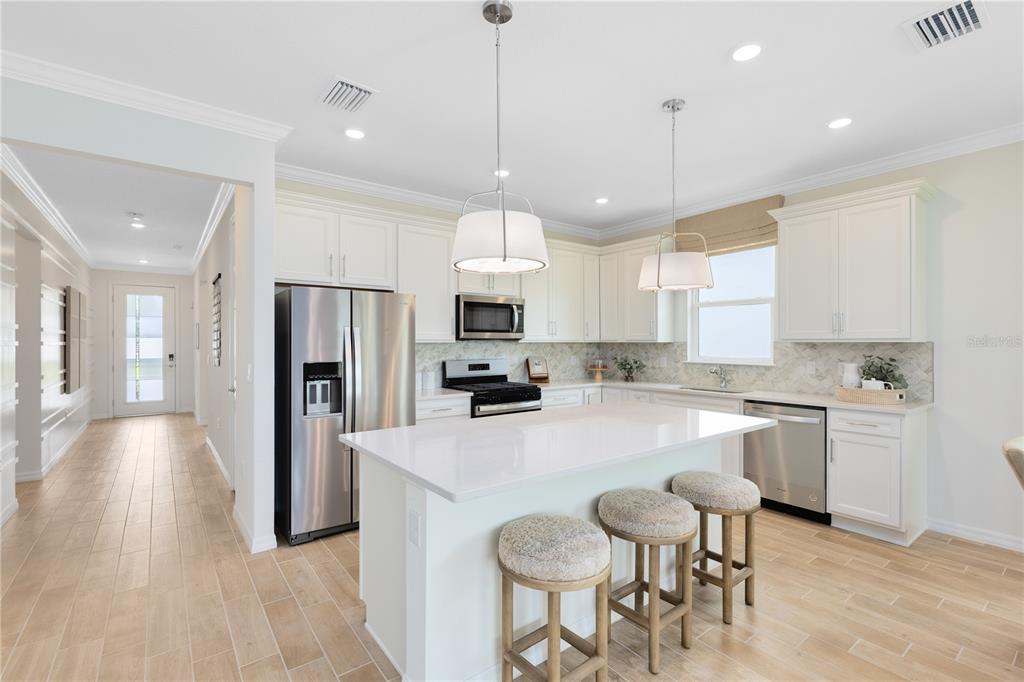 A bright kitchen features white cabinetry, a central island with bar stools, and stainless appliances — 16207 TROPICAL SAGE DRIVE, ORLANDO, FL