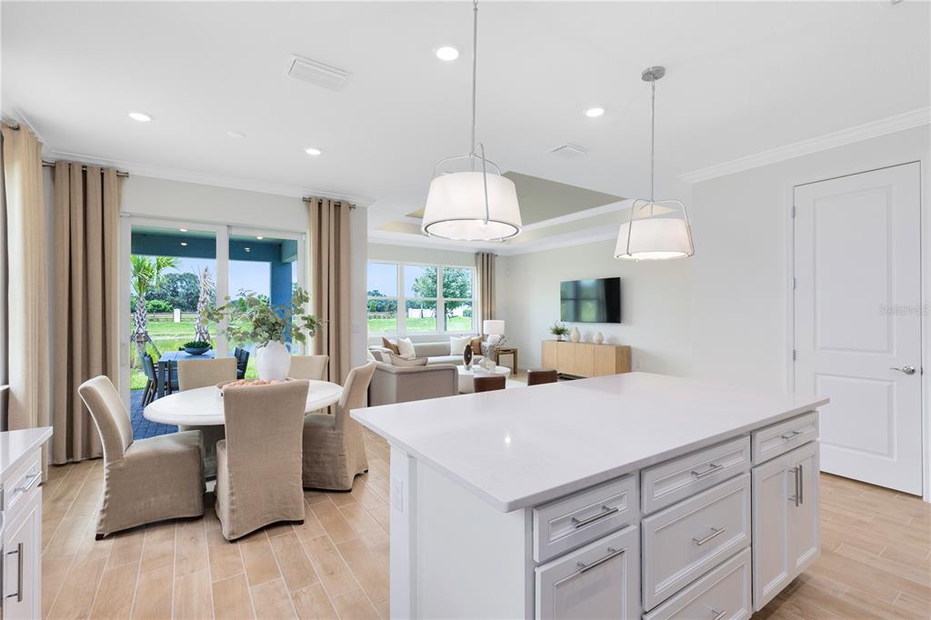 A bright, open-concept kitchen and dining area features a white island, pendant lighting, and tile flooring — 16207 TROPICAL SAGE DRIVE, ORLANDO, FL