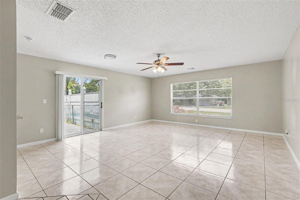 A spacious living room features light-colored tile flooring, neutral walls, a ceiling fan, and sliding doors — 483 WATER RUN, OCALA, FL