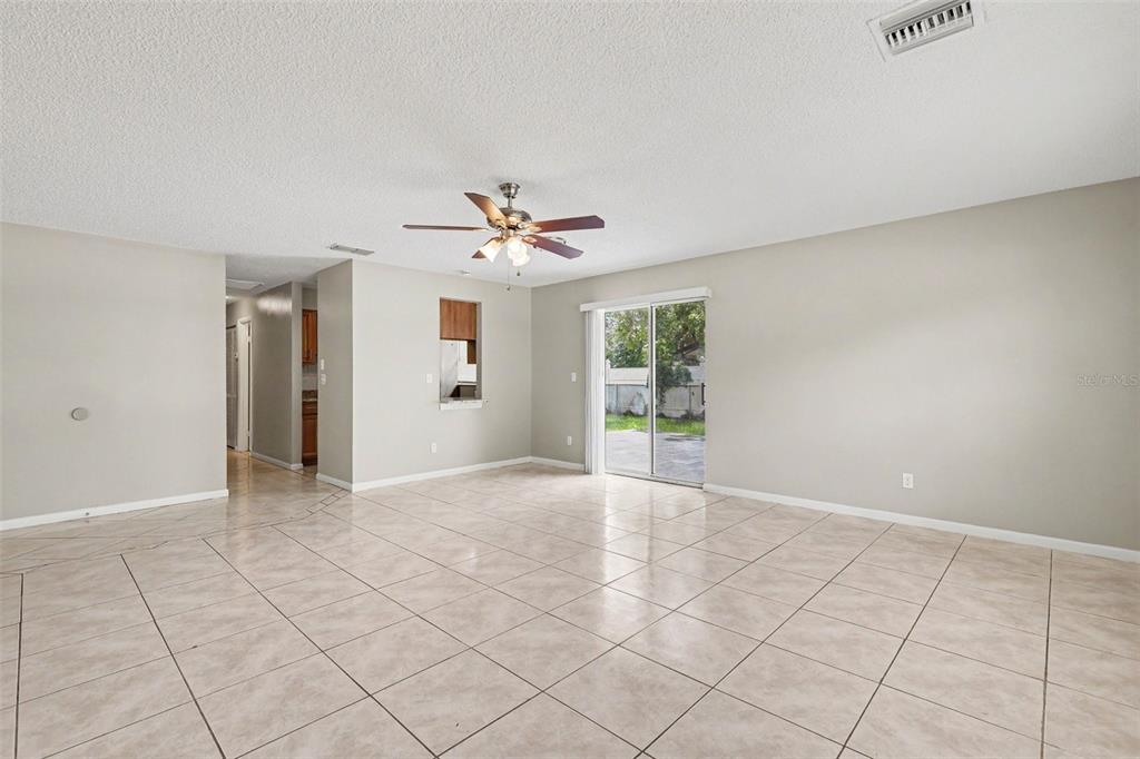 An open living area features light-colored tile flooring, a ceiling fan, and sliding glass doors — 483 WATER RUN, OCALA, FL