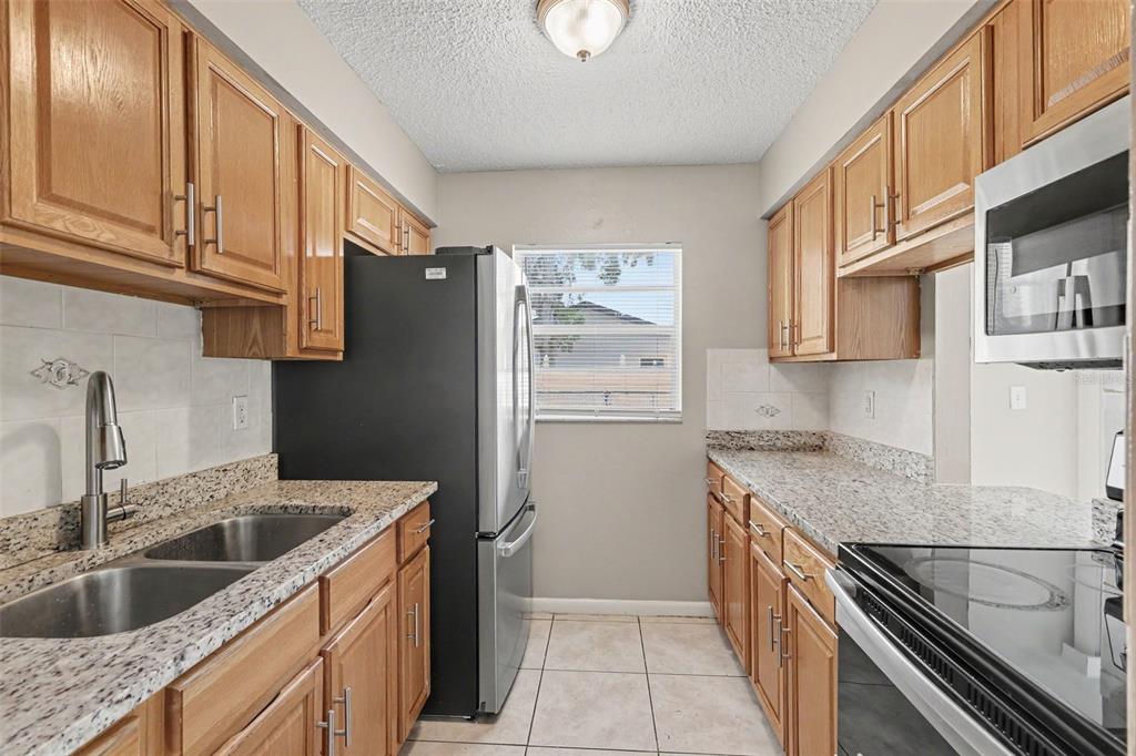 A galley kitchen features light wood cabinets, granite countertops, stainless steel appliances, and tile flooring — 483 WATER RUN, OCALA, FL