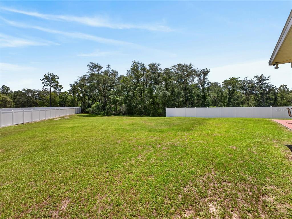 A large, grassy backyard is enclosed by white vinyl fencing and bordered by mature trees — 417 RIO GRANDE COURT, KISSIMMEE, FL