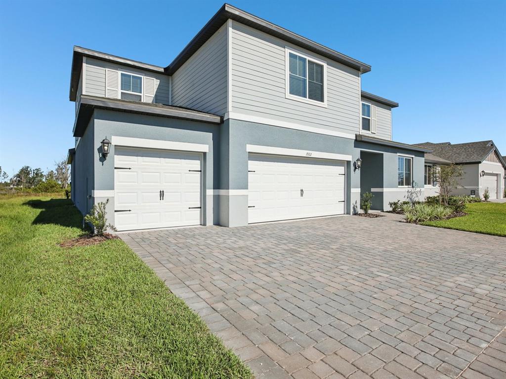 A two-story house features a three-car garage, gray siding, and a paved driveway — 1922 COOLRIDGE PLACE, ZEPHYRHILLS, FL