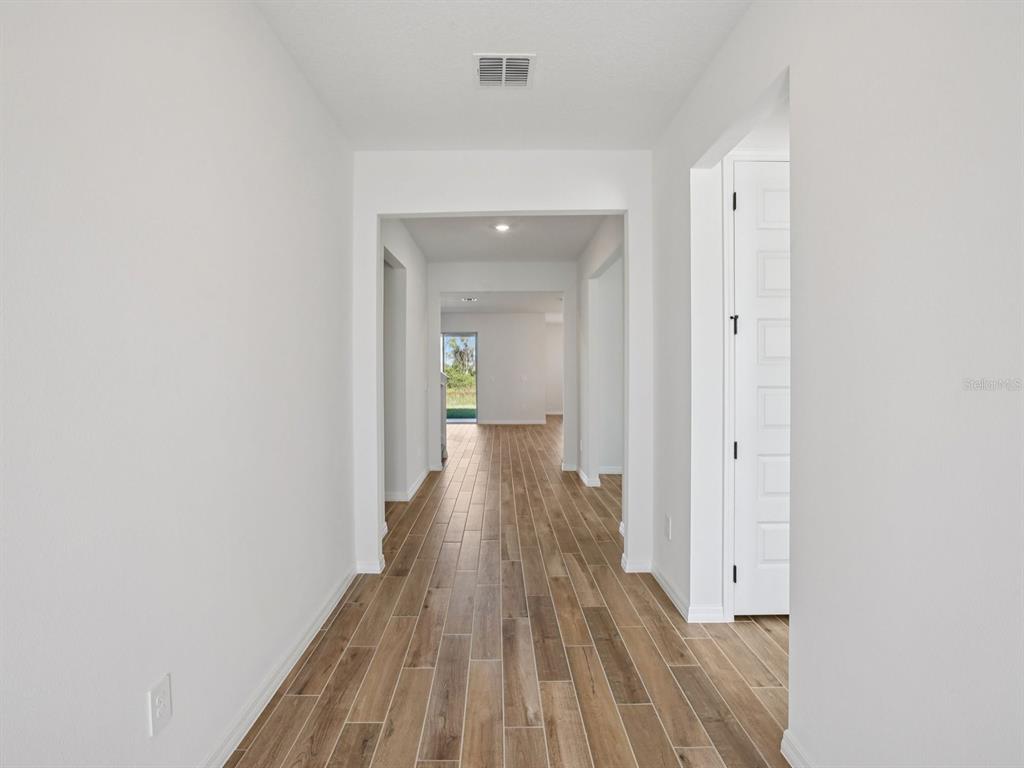 A bright hallway features white walls, wood-look tile flooring, and a doorway leading outside — 1922 COOLRIDGE PLACE, ZEPHYRHILLS, FL