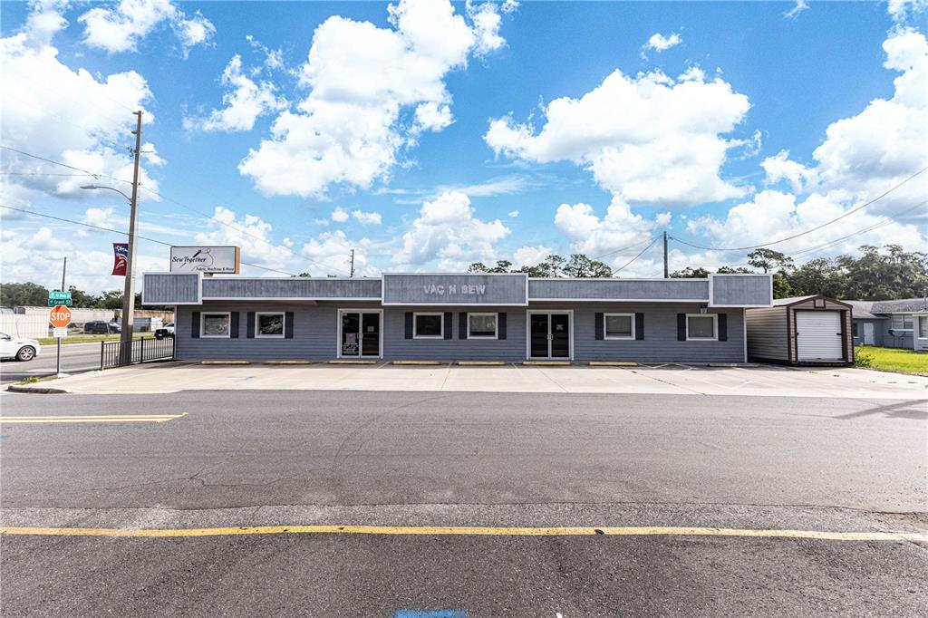 A single-story commercial building with gray siding and a parking lot sits under a blue sky — 700 N MAIN STREET, WILDWOOD, FL