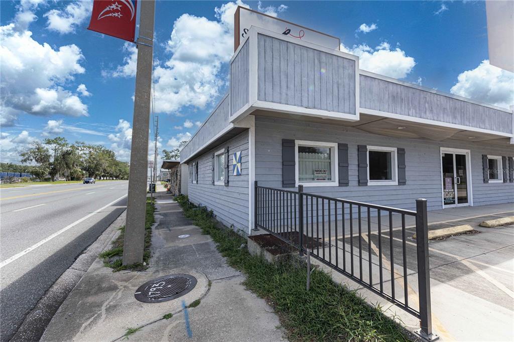 A gray, single-story commercial building with a metal fence and sidewalk along a road — 700 N MAIN STREET, WILDWOOD, FL