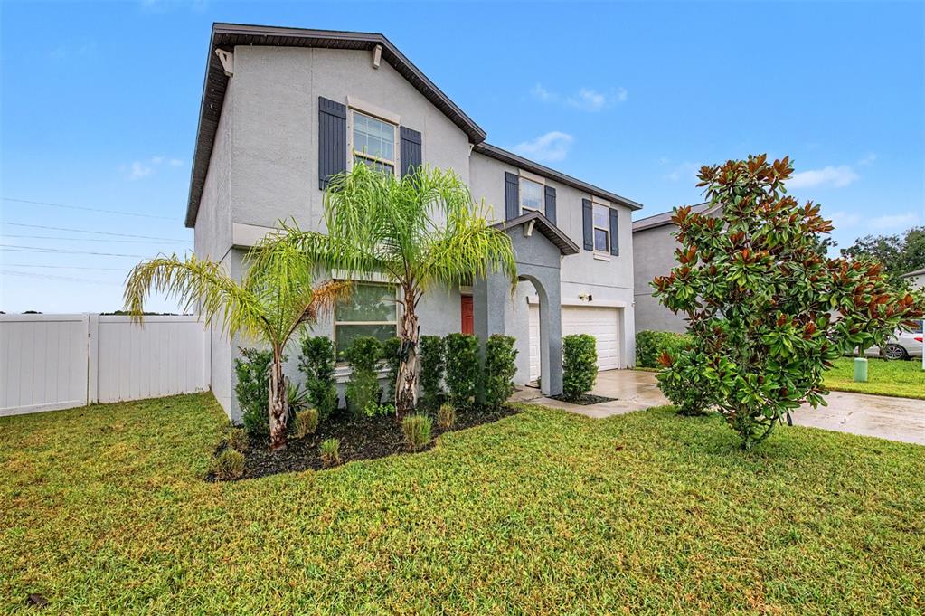 A two-story suburban house with a gray stucco exterior, a palm tree, and a lawn — 4710 WILD SENNA BOULEVARD, TAMPA, FL