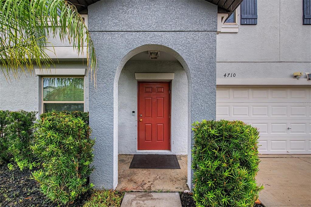 A red front door is centered under an arched entryway next to a garage — 4710 WILD SENNA BOULEVARD, TAMPA, FL