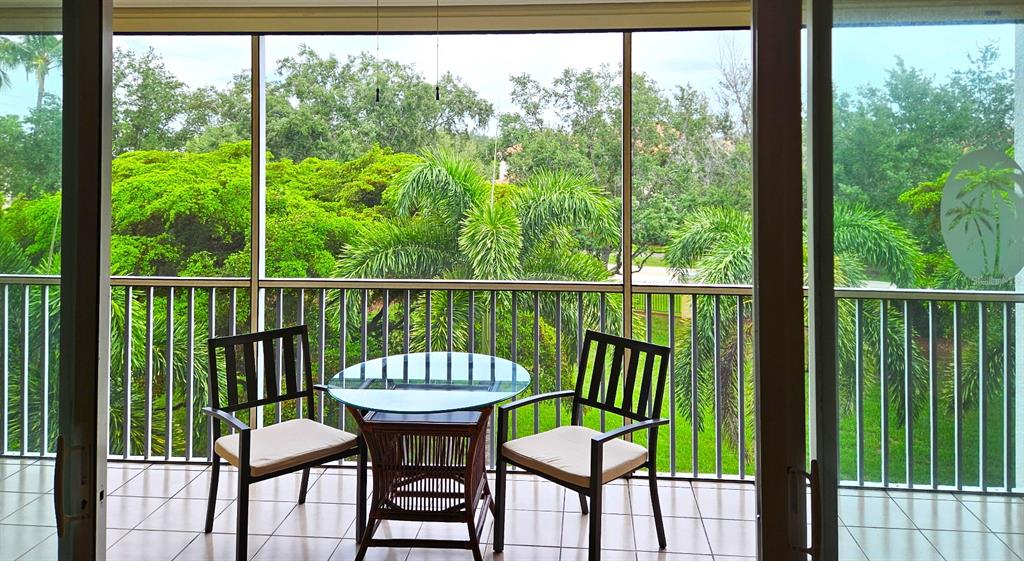 A screened-in balcony features a glass-topped table and two chairs overlooking lush tropical greenery — 255 W END DRIVE UNIT 4308, PUNTA GORDA, FL