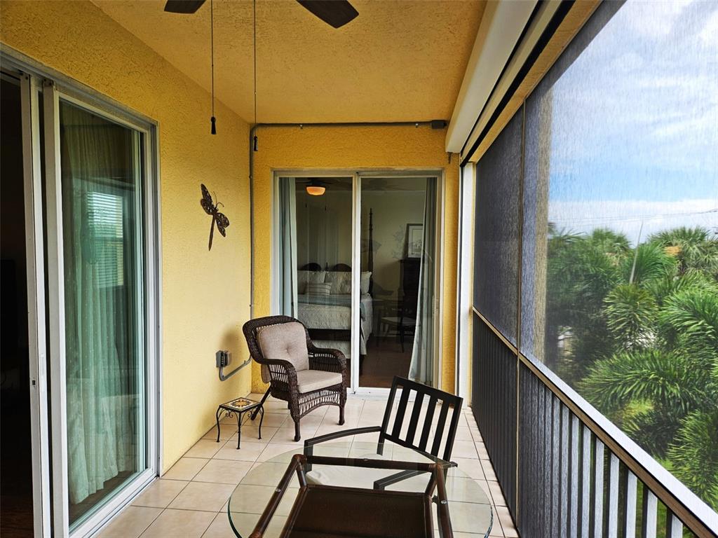 A screened-in balcony features tile flooring, wicker furniture, and a view of palm trees — 255 W END DRIVE UNIT 4308, PUNTA GORDA, FL