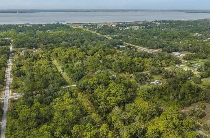 An aerial view shows a wooded lot with a road, nearby houses, and a large lake — INDIAN LAKE DRIVE, INDIAN LAKE ESTATES, FL