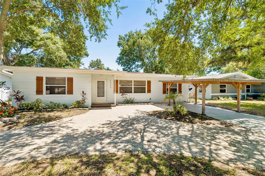 A single-story house with white siding, brown shutters, and a paved driveway with a carport — 1555 MAGNOLIA DRIVE, CLEARWATER, FL