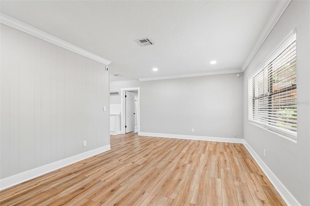 An empty room features light gray walls, wood-look flooring, crown molding, and a large window — 1555 MAGNOLIA DRIVE, CLEARWATER, FL