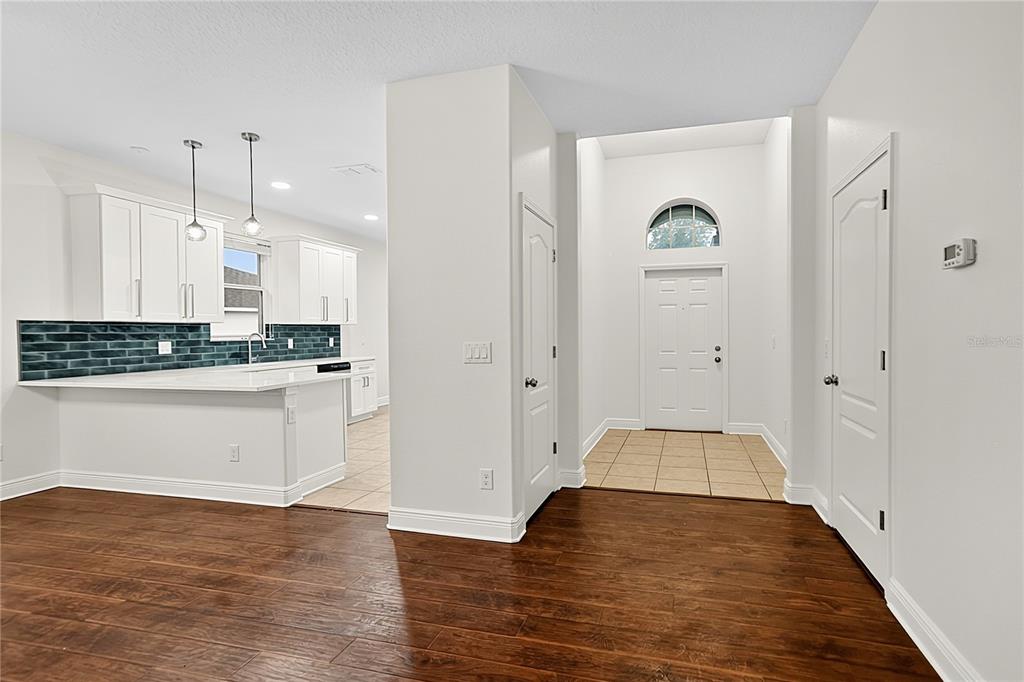 A view from a wood-floored room toward a tiled entryway and a white kitchen — 5708 RUTHERFORD ROAD, MOUNT DORA, FL