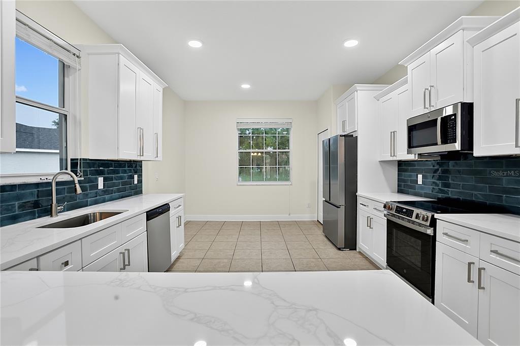 A kitchen features white cabinetry, marble-look countertops, a dark blue tile backsplash, and stainless appliances — 5708 RUTHERFORD ROAD, MOUNT DORA, FL