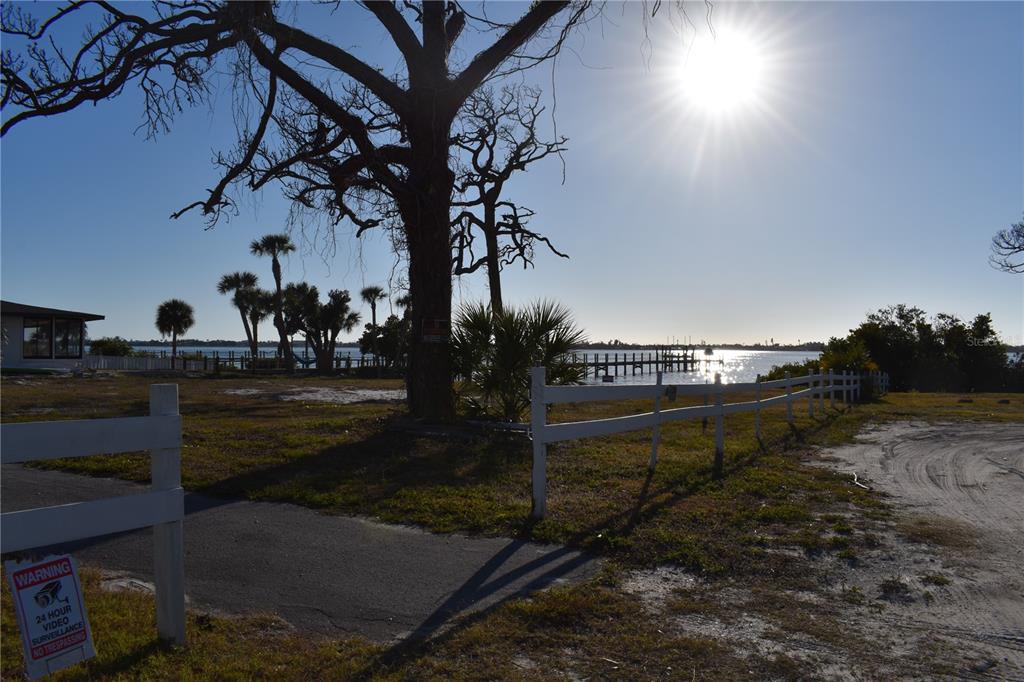 A large tree stands on a sandy lot overlooking a waterfront dock under bright sun — 175 W BAY STREET, ENGLEWOOD, FL