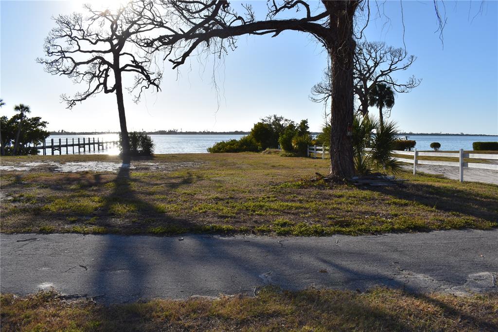 A grassy waterfront lot features two large trees and a white fence near the water — 175 W BAY STREET, ENGLEWOOD, FL