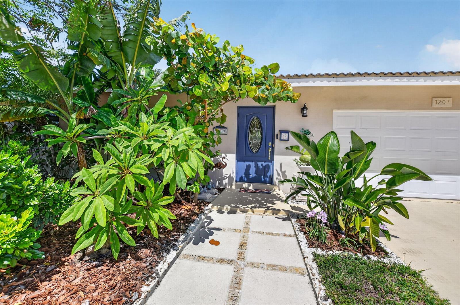 A blue front door is surrounded by lush tropical landscaping and a concrete walkway — 1207 SW 12th Avenue, Boca Raton FL 33486, BOCA RATON, FL