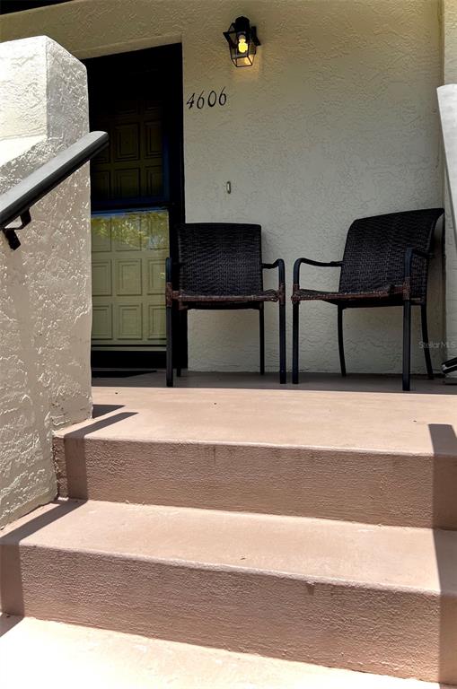 Two dark wicker chairs sit on a concrete porch in front of a dark door — 4606 WEYBRIDGE UNIT 26, SARASOTA, FL
