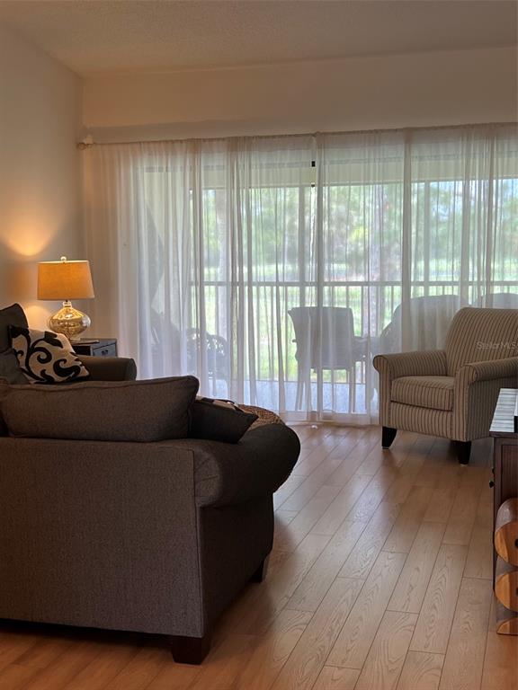 A living room features light wood flooring, a dark sofa, and a striped armchair — 4606 WEYBRIDGE UNIT 26, SARASOTA, FL