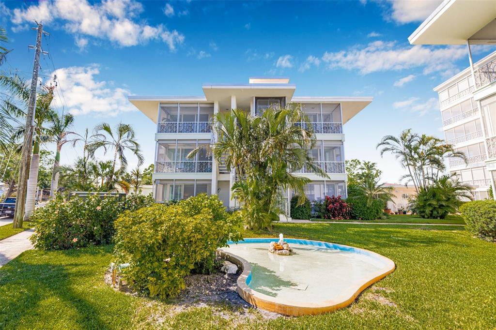 A three-story apartment building with screened balconies sits behind a small fountain and lawn — 615 10TH AVENUE NE UNIT 1, ST PETERSBURG, FL