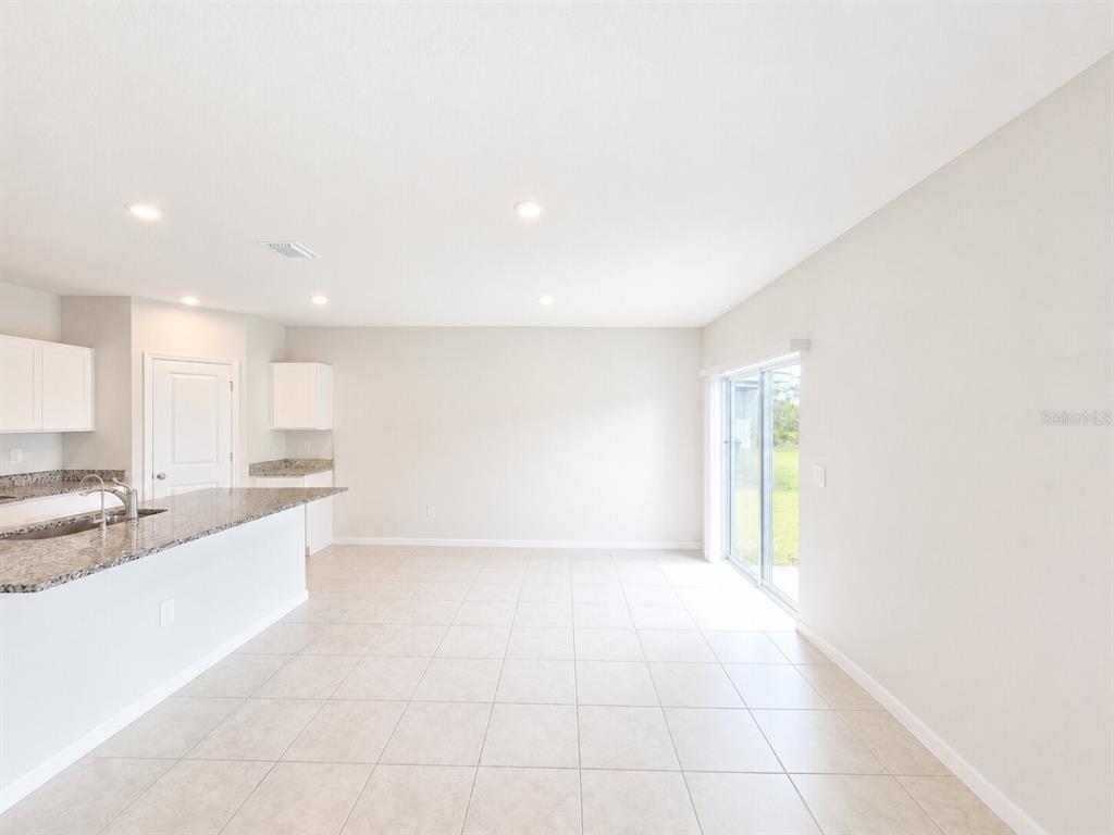 A kitchen with granite countertops and tile flooring opens into a bright, empty living area — 810 172ND COURT E, BRADENTON, FL