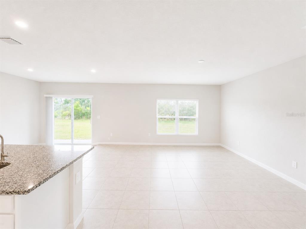 An open-concept living area features light-colored tile flooring, white walls, and a sliding glass door — 810 172ND COURT E, BRADENTON, FL